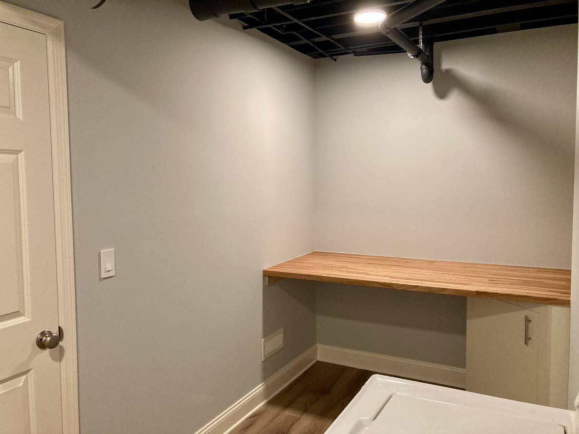 A fourth photo of the laundry room from a fourth angle. The butcher block shelf is again visible on the far wall.