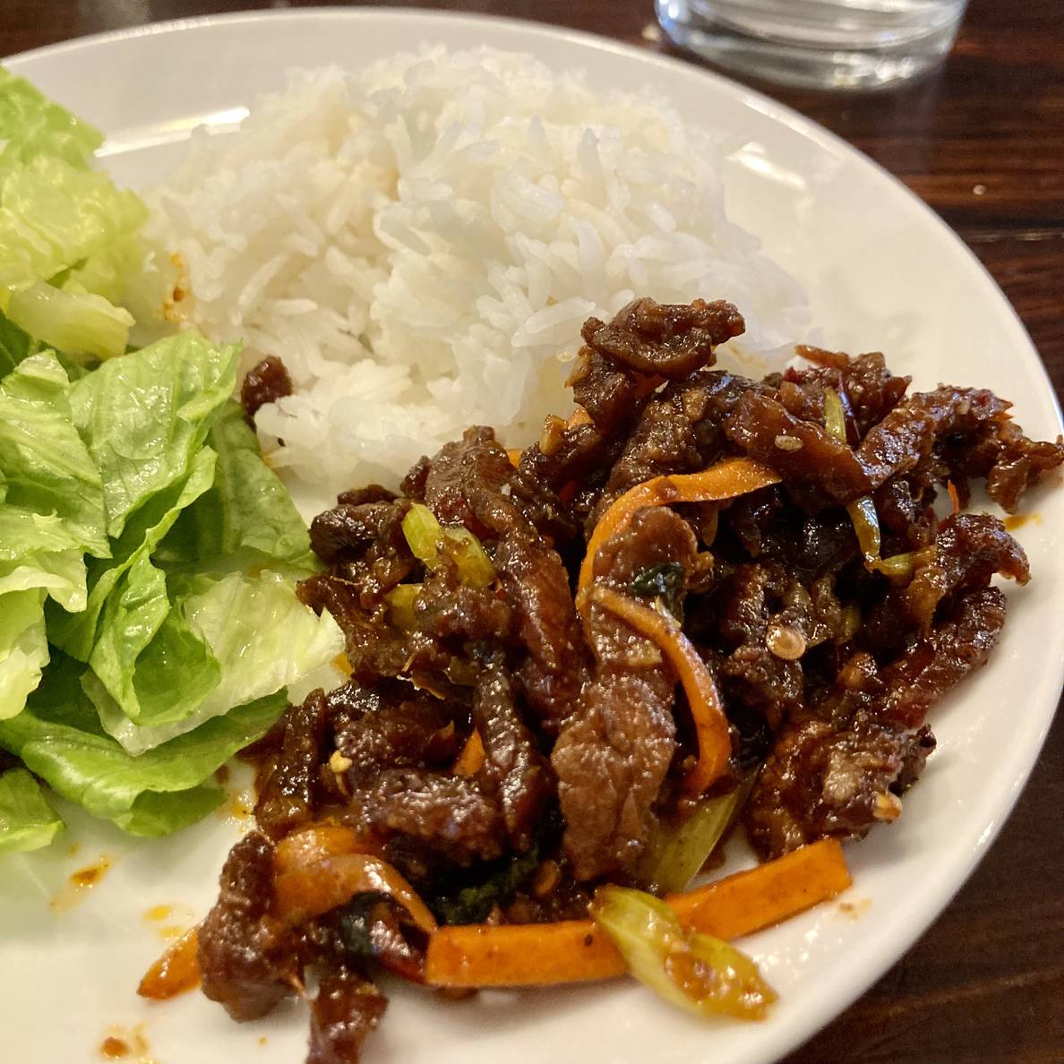 A photo of the sichuan dry-fried beef plated with some rice and salad.