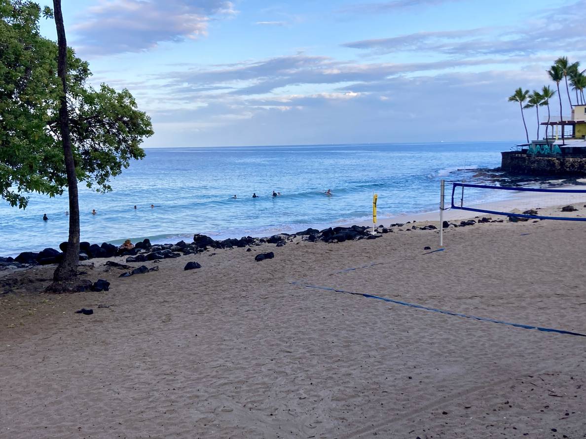 A photo of a Hawaiian beach. The water is dotted with boogie boarders.