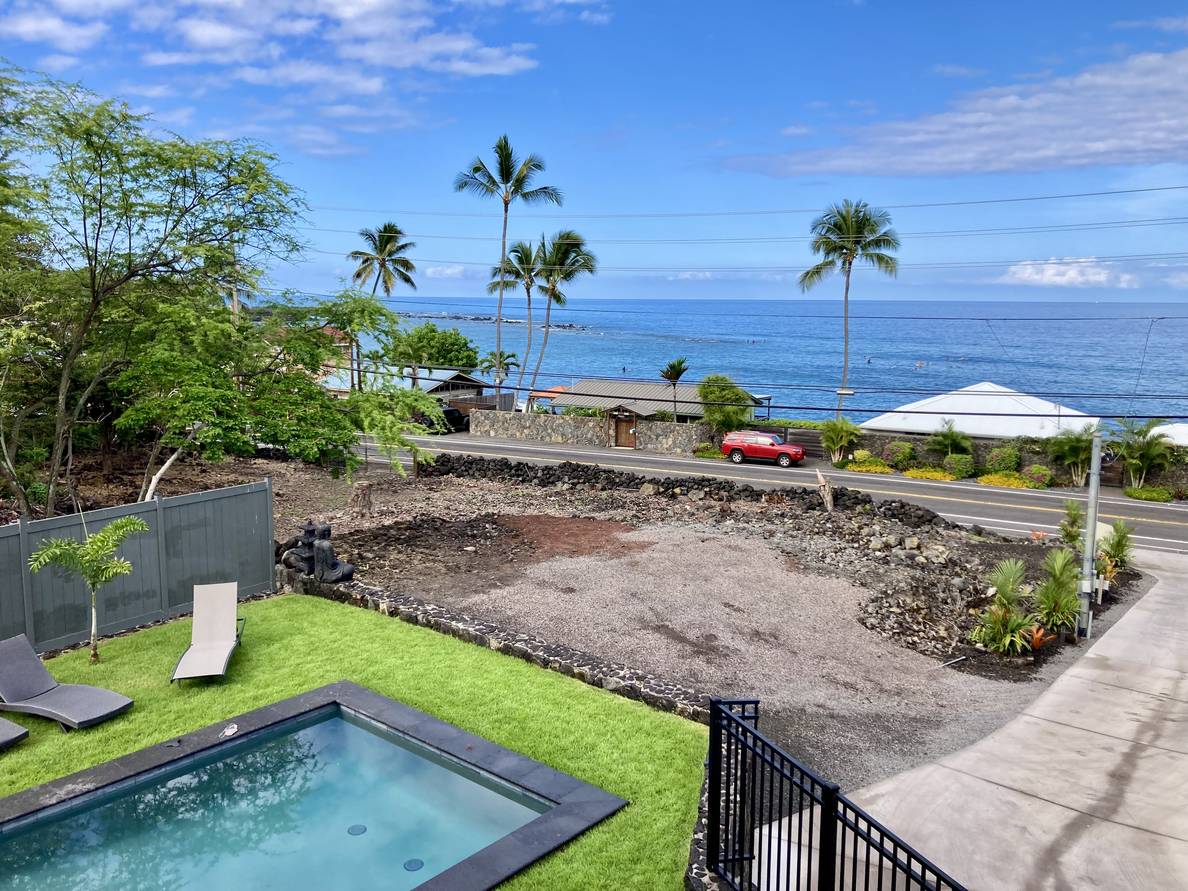 A photo of from our Airbnb balcony. The sky has wisps of clouds. Palm trees flank the left of the frame. Surfing lessons are happening in the ocean below.