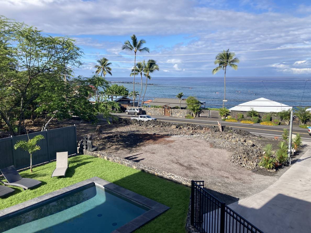 A photo from our Airbnb balcony. The sky has fluffy clouds and the ocean is relatively calm. Some surgeries are in the water. Palm trees are on the left.