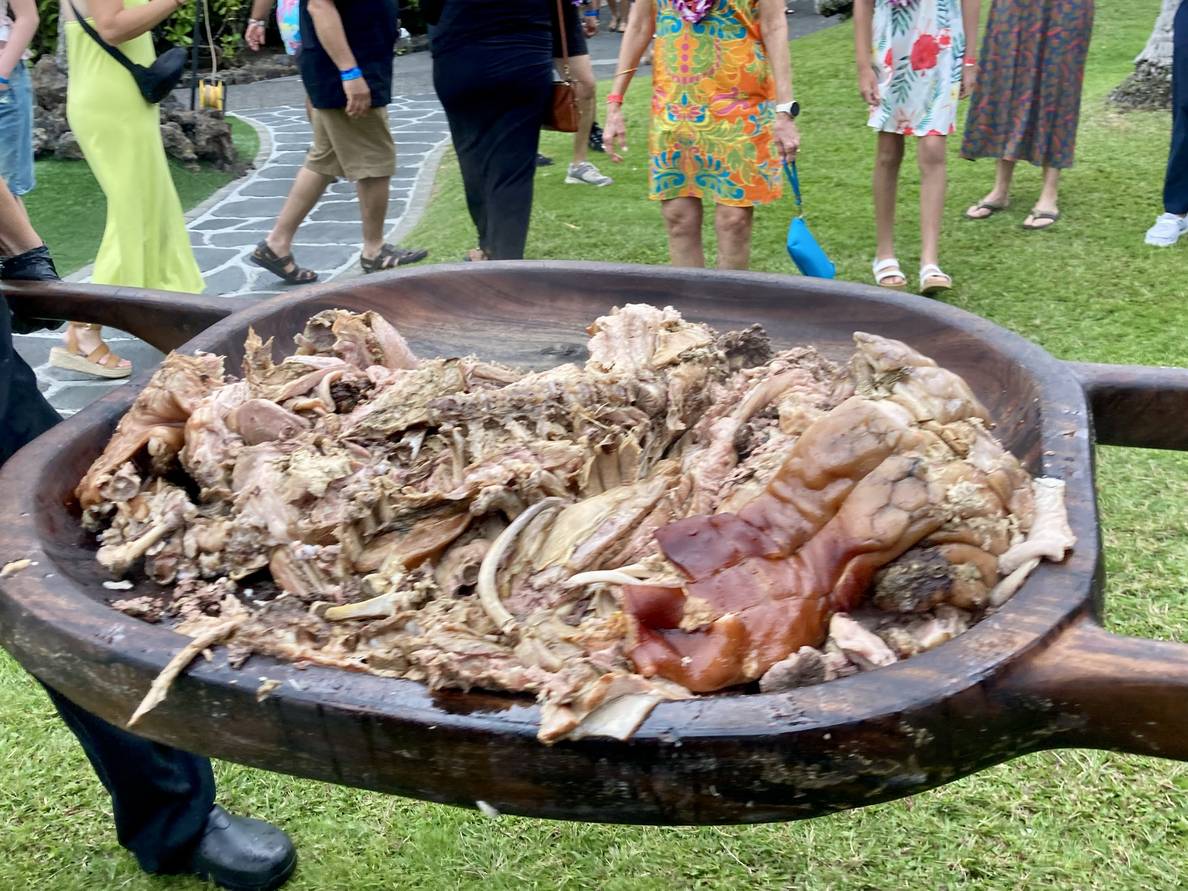 A photo of a cooked pig on a large tray being carried by two people.