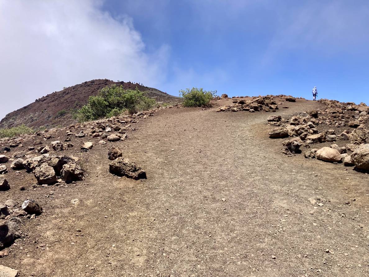 A photo of a scree trail to a summit. A person in the distance is halfway up.