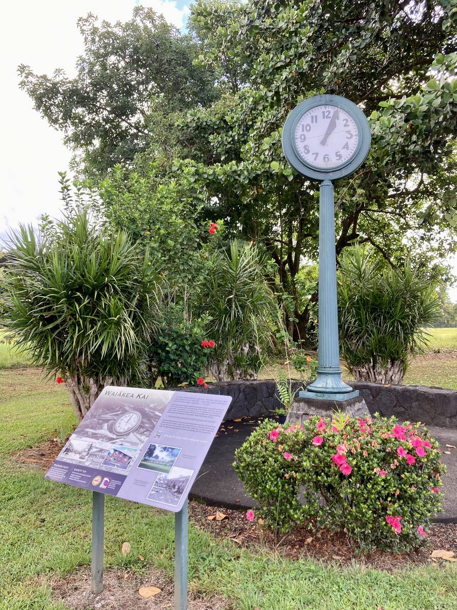 A photo of a town clock and an info board. The time on the analog clock is 1:04.