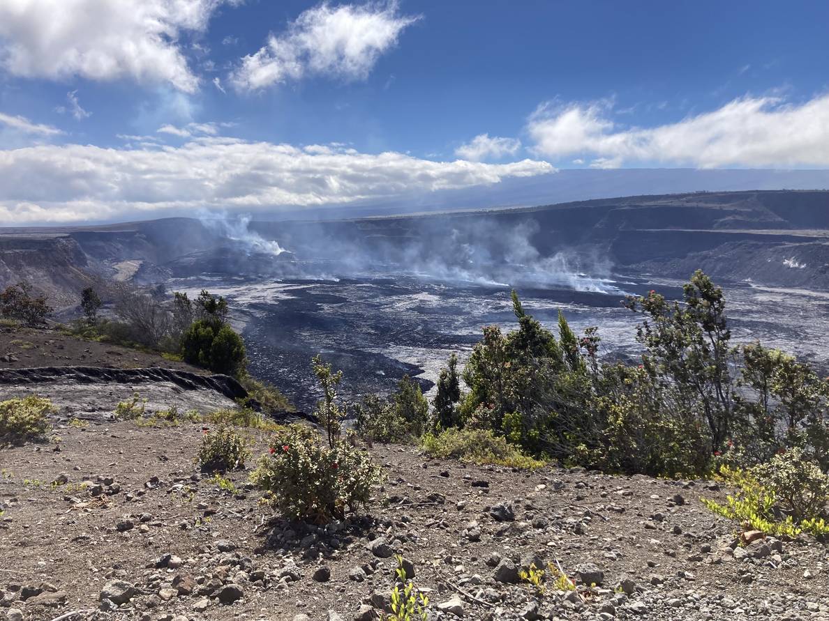 A photo of a volcanic crater. Steam rises from multiple sites in the crater.