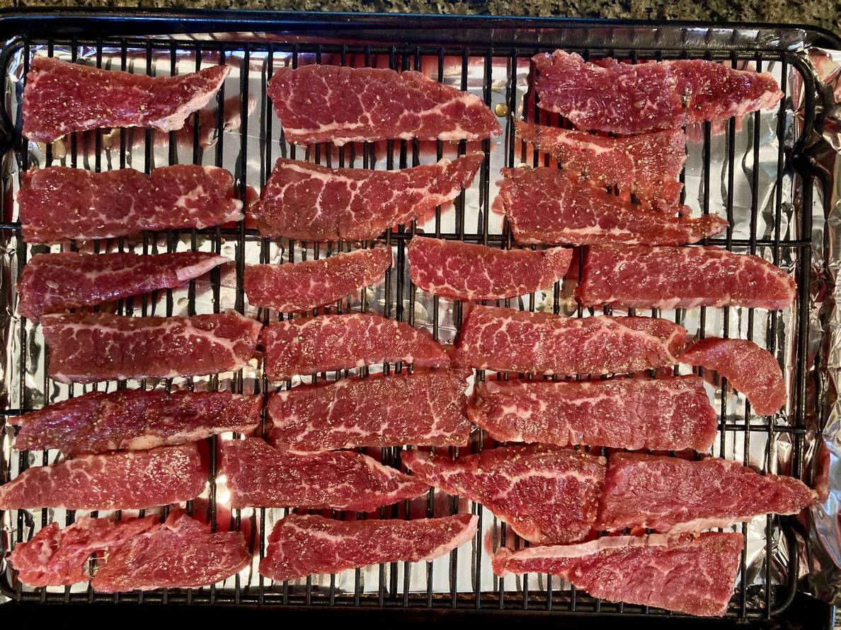 A photo of half-inch slices of beef on a wire rack inside a sheet pan.
