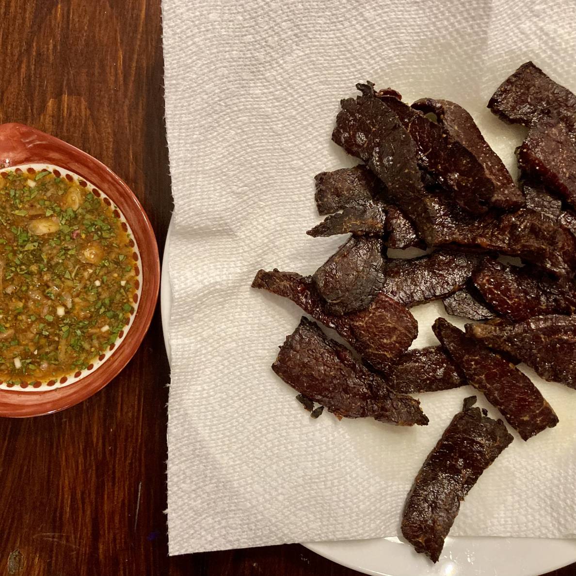 A photo of fried beef strips on a paper-towel-lined plate. Next to it is a shallow bowl of dipping sauce.