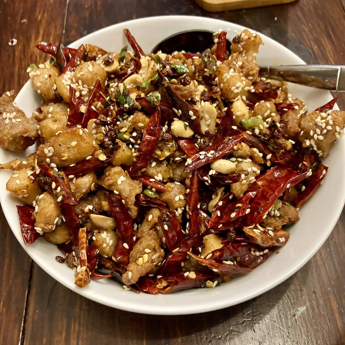 A photo of a bowl of small pieces of fried chicken mixed with red dried chiles and a bunch of sesame seeds.