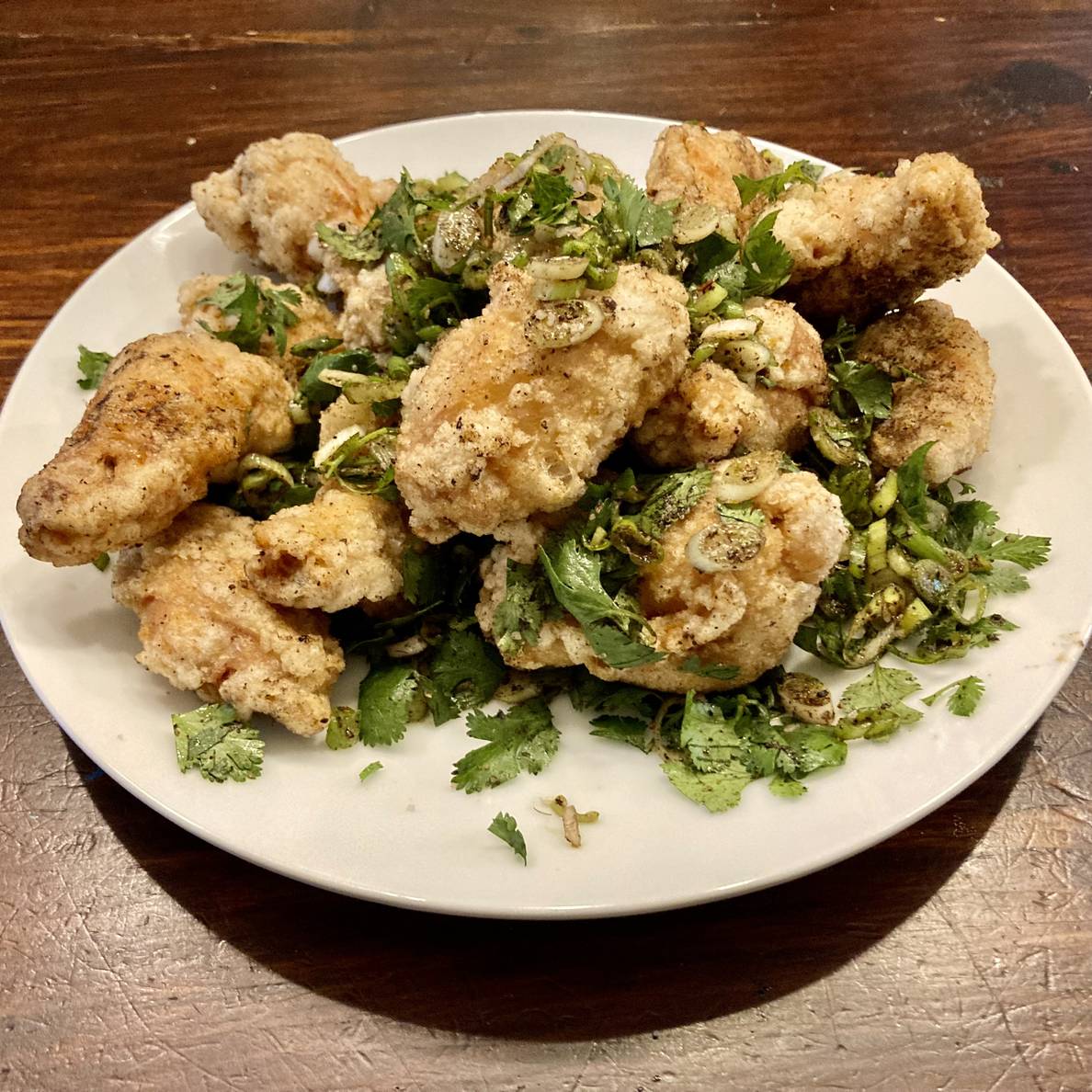 A photo of fried chicken wings tossed with green onions, cilantro, and a toasted hot and numbing spice blend.