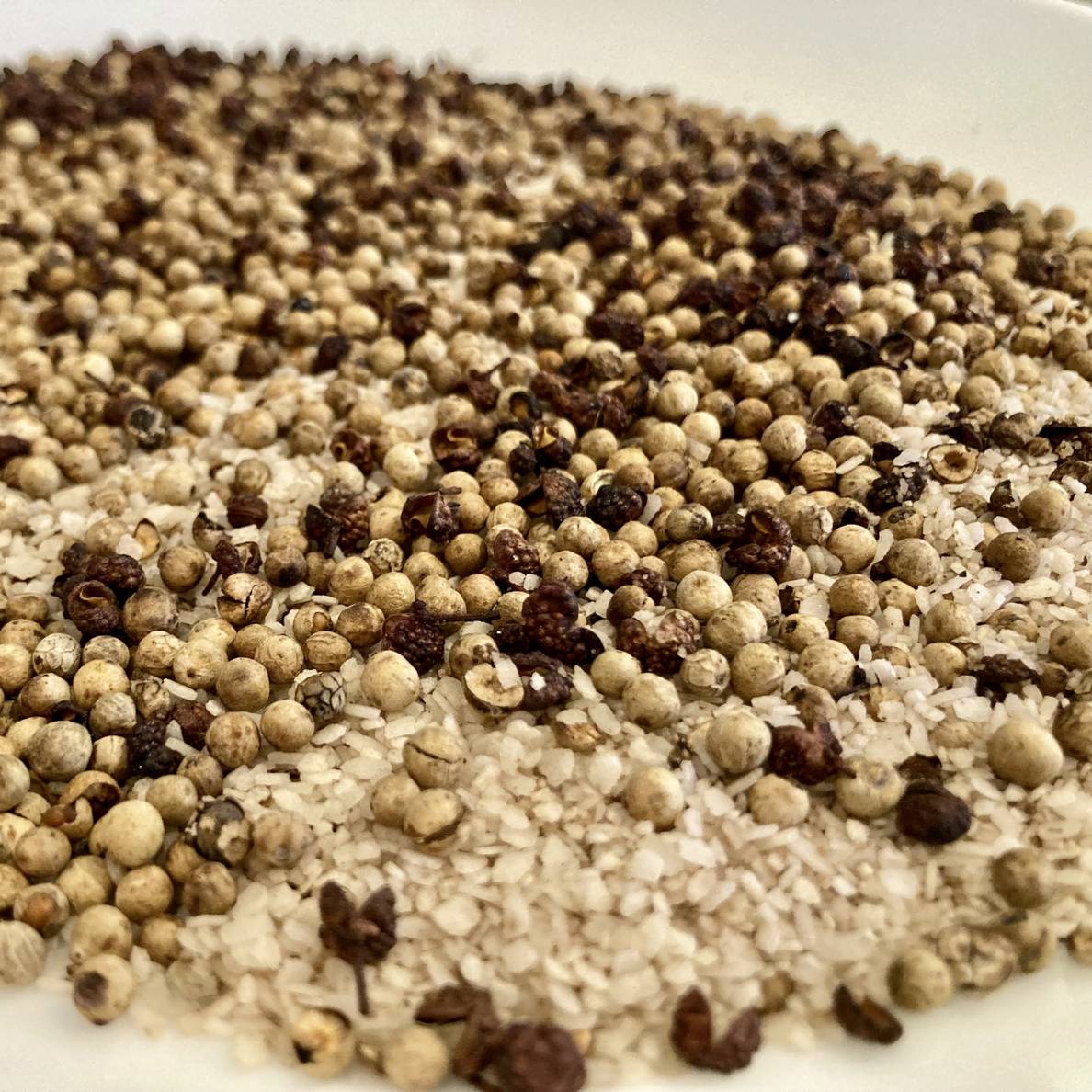 A photo of a plate of toasted salt, white pepper corns, and Sichuan peppercorns.