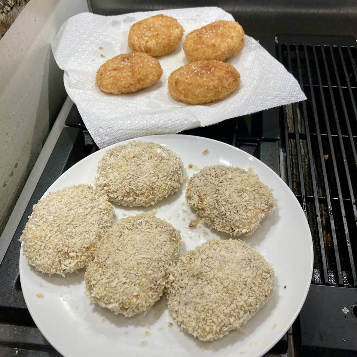 A photo of two plates of korokke. One is golden brown on a paper towel. The other is obviously not yet fried from it’s pale color.