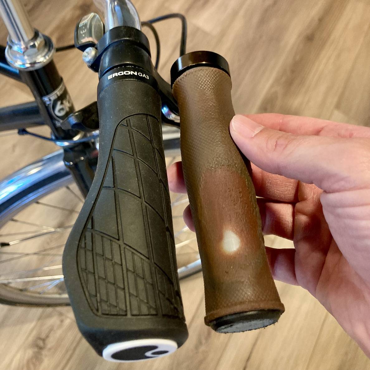 A photo of a bicycle handlebars with new grips and a hand holding old worn out grips next to it.