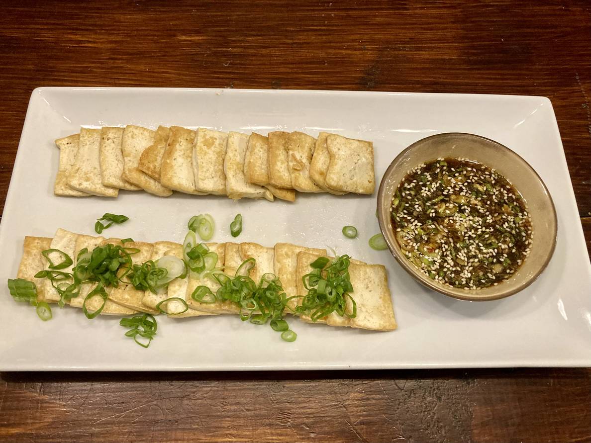 A photo of the final dish on a serving platter. The tofu slices are in two rows, one sprinkled with scallions. A bowl of the dipping sauce is at one end of the platter.