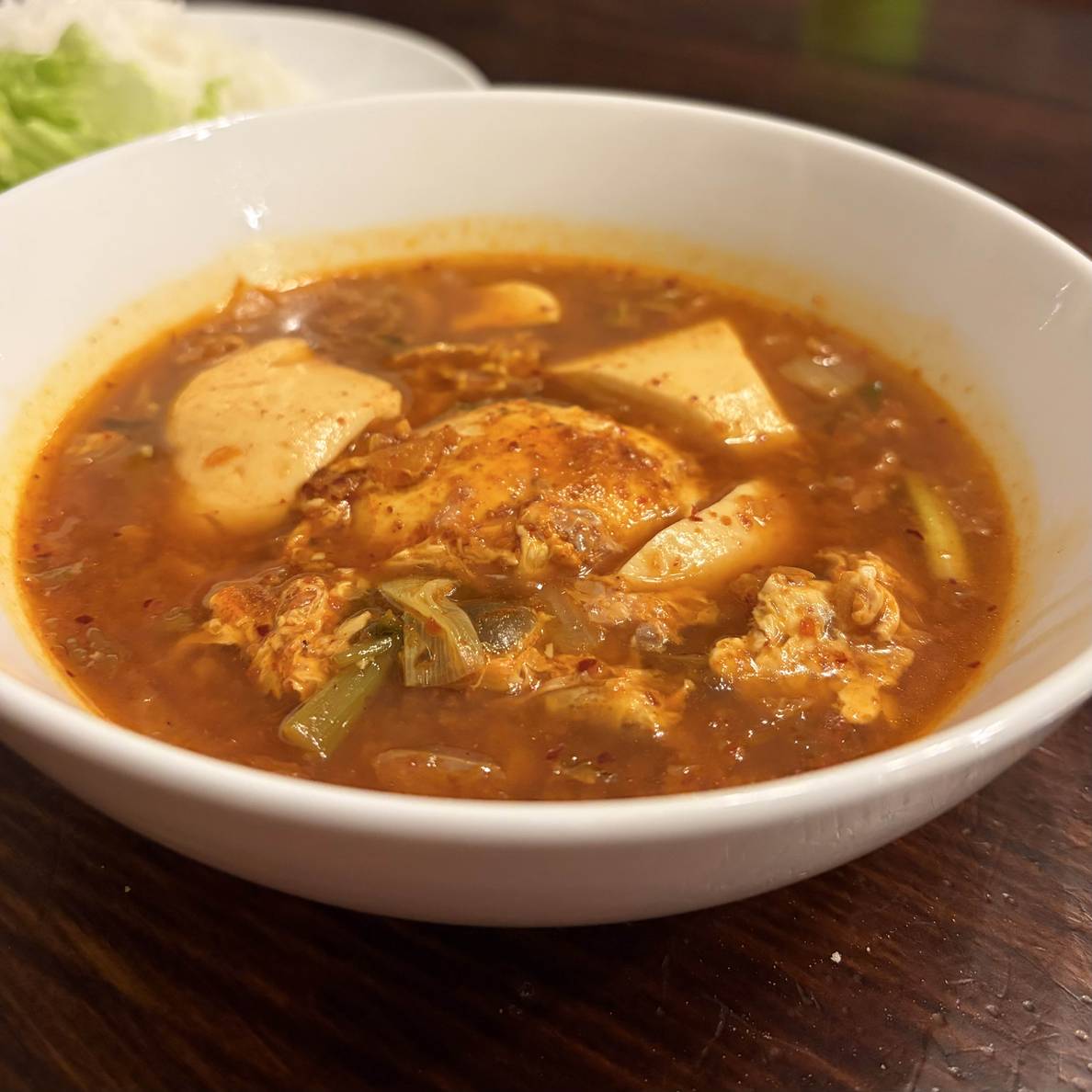 A photo of a bowl of the finished soup. The poached egg is in the middle with large chunks of soondubu around it in a soup broth.