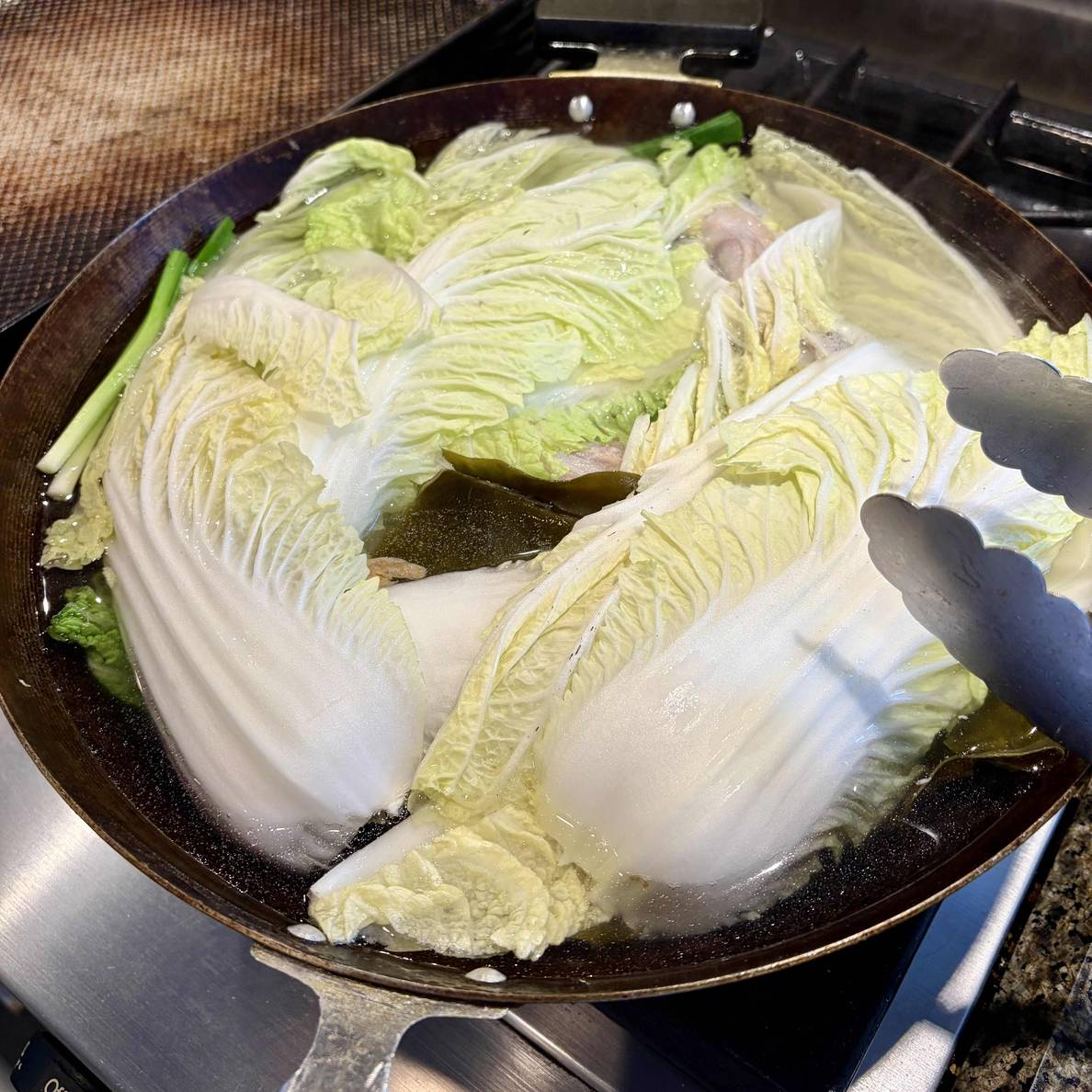 A photo of the all of the ingredients in the wok. Everything is under napa cabbage leaves.