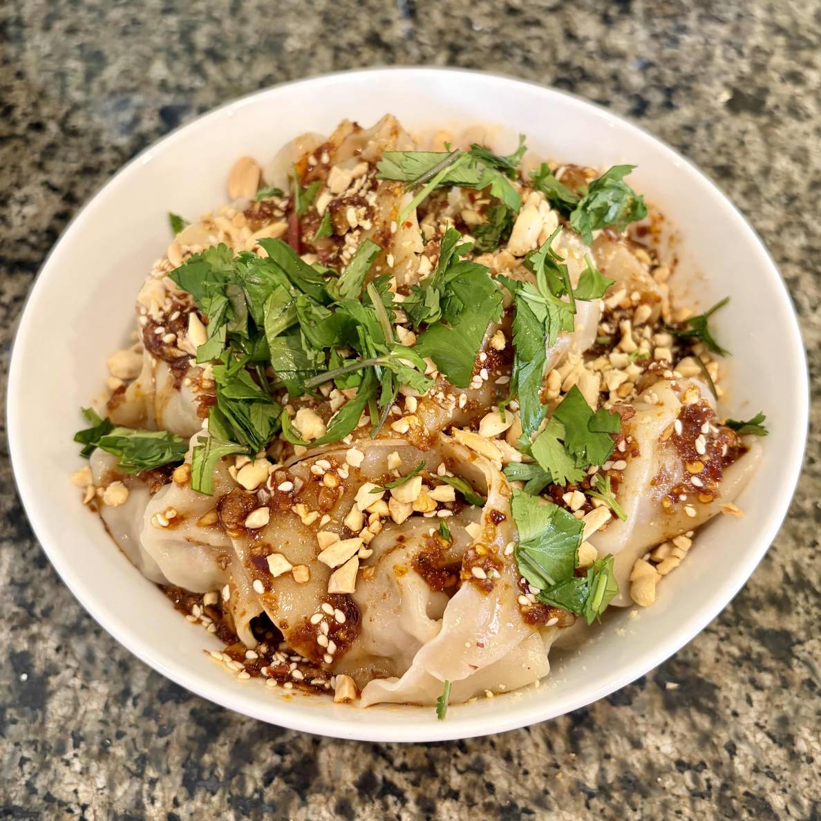 A photo of a bowl of the finished wontons. The hot and sour sauce coats all of the pieces and cilantro and peanuts are sprinkled on top.