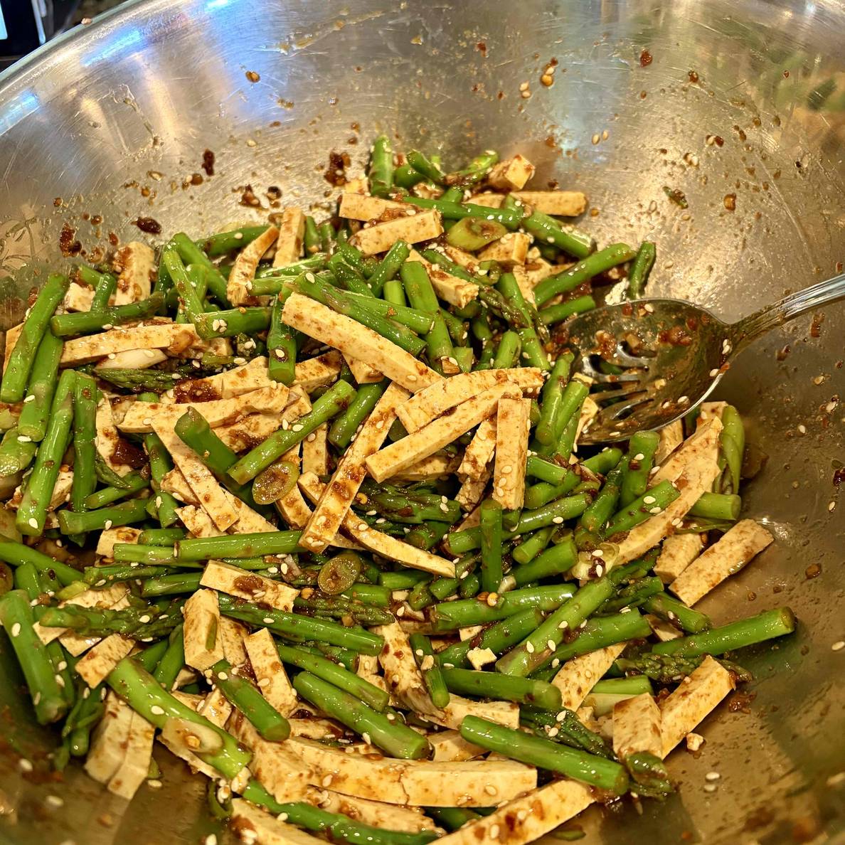 A photo of the salad after tossing with the dressing. The asparagus and tofu matchsticks are similar sizes and covered in the sauce.