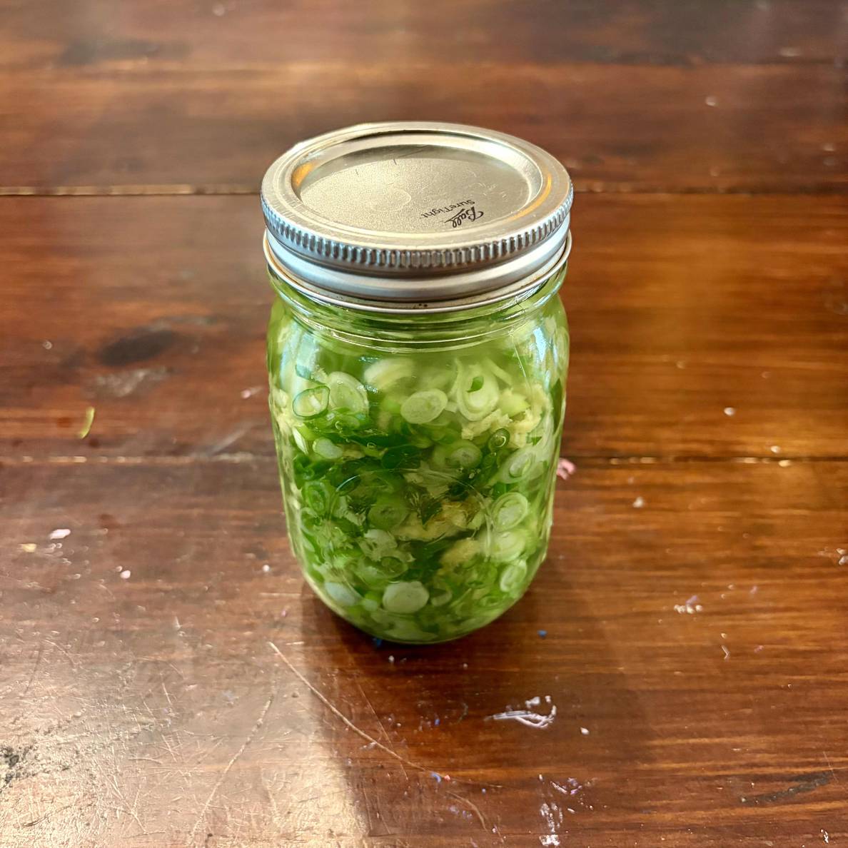 A photo of the jar of finished sauce. It is packed to the lid with scallion slices.